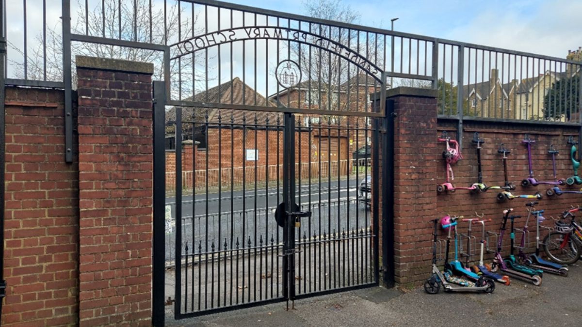 A metal school gate in a brick wall, with scooters parked alongside