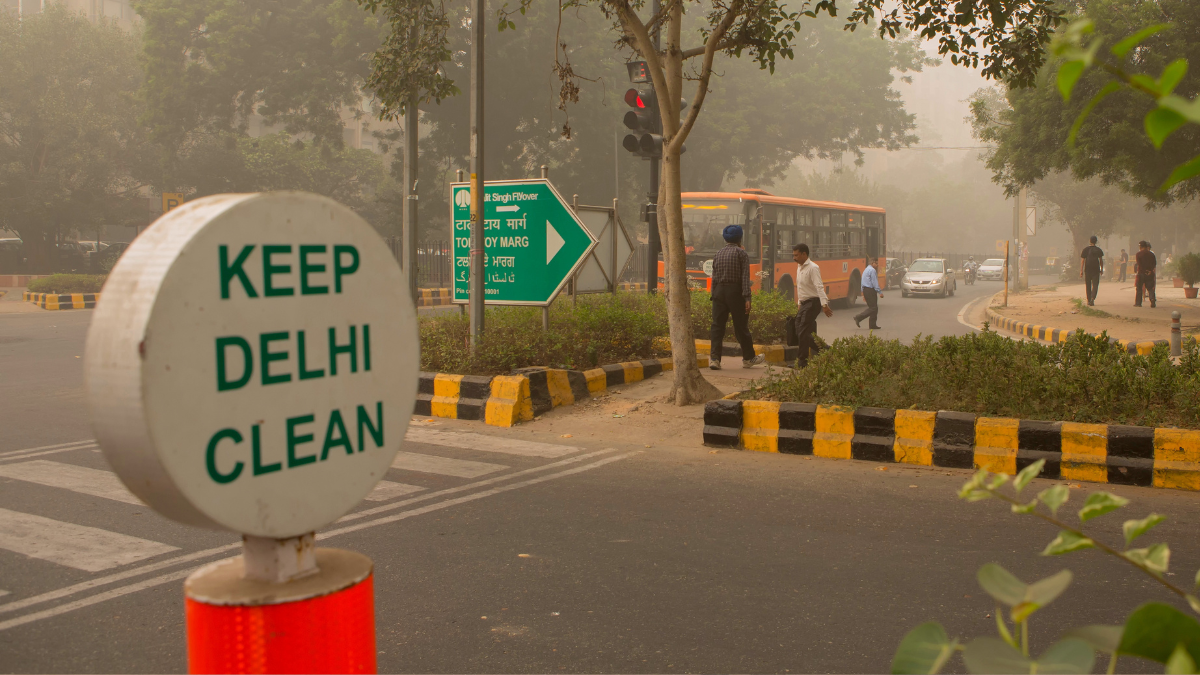 Sign saying "keep delhi clean" at a polluted intersection