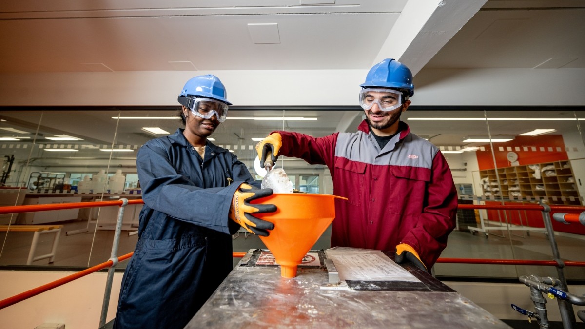 Two students in safety gear, including hard hats and glasses, are diligently working on a project in the University's Chemical Engineering lab