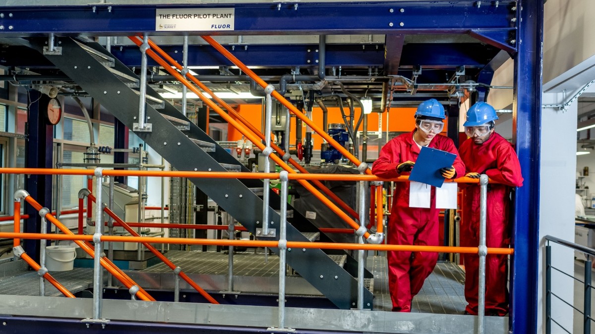 2 students in engineering overalls and hard hats suits are working together in the University's Pilot Plant
