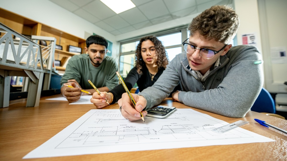 Three students are collaborating on an engineering drawing 