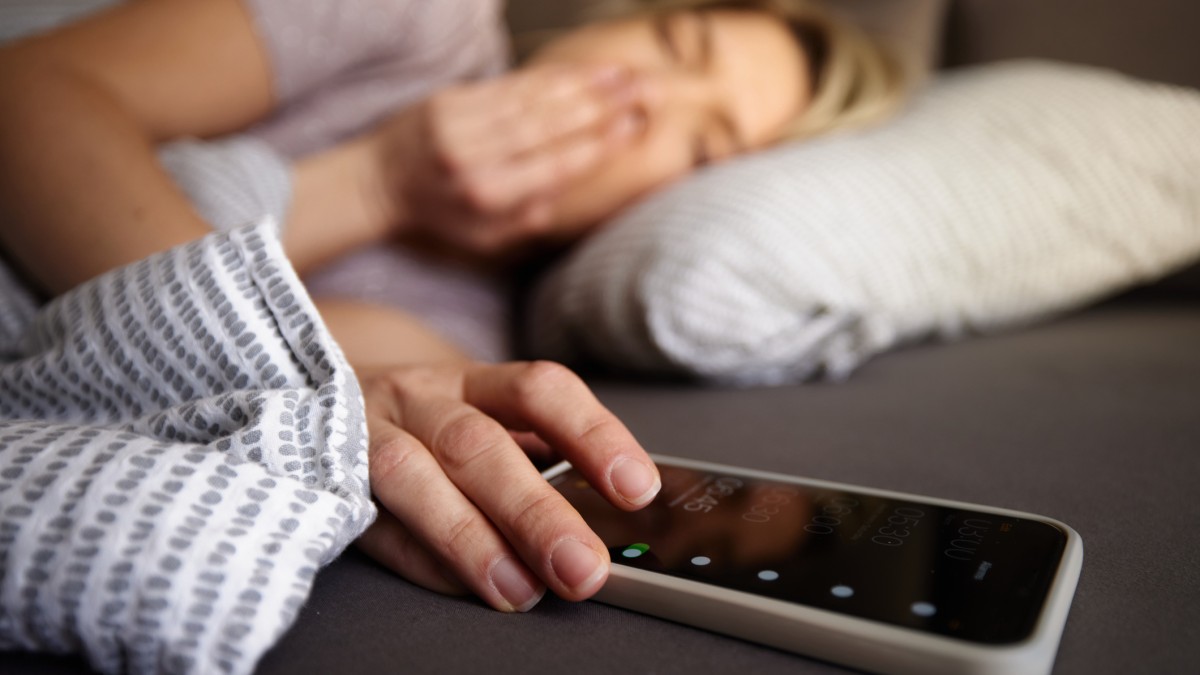 Close up of a woman turning off her alarm clock on smart phone while waking up in a bed.