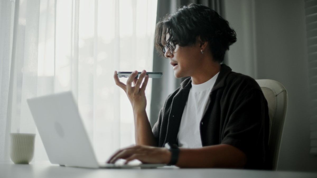 Male student using ai voice assistant while working with laptop.