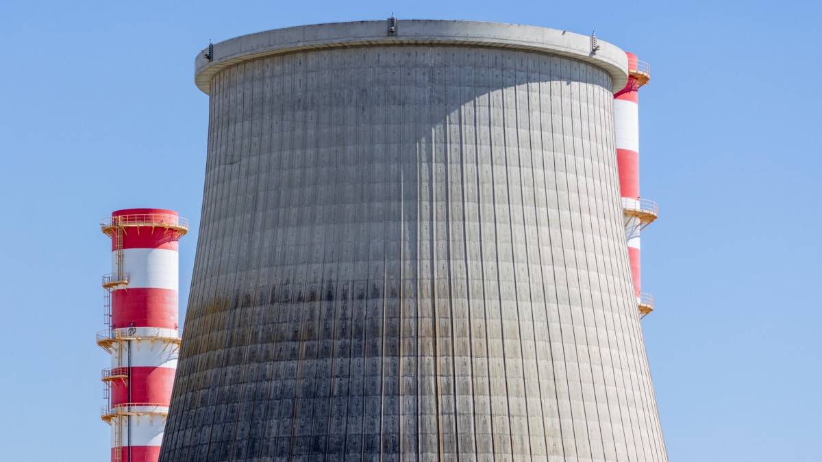 Large concrete cooling tower and red and white chimney of the carregado thermoelectric power plant in Portugal, under a clear blue sky