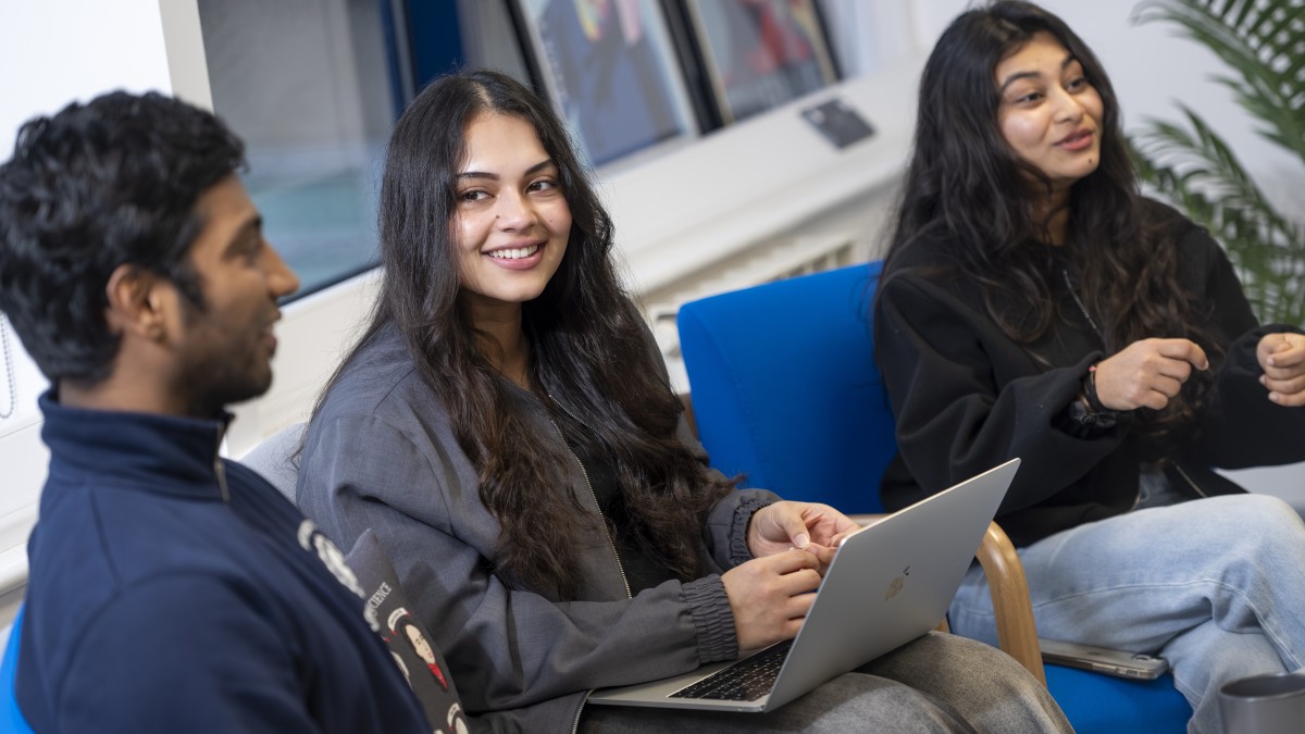 Three students sit together on chairs having a chat.