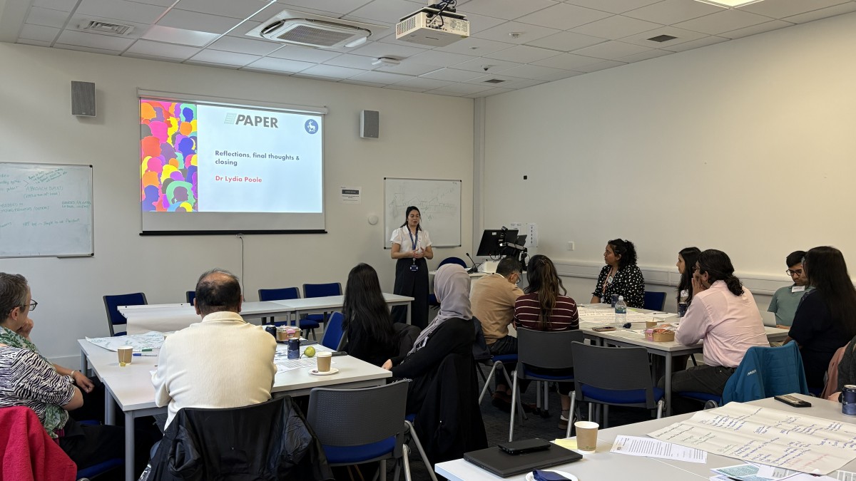 Groups of people sit in a seminar room facing a projection on the wall.