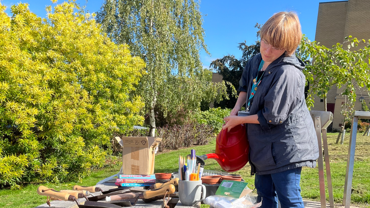 Staff member leading a gardening session waters seeds on a wooden bench