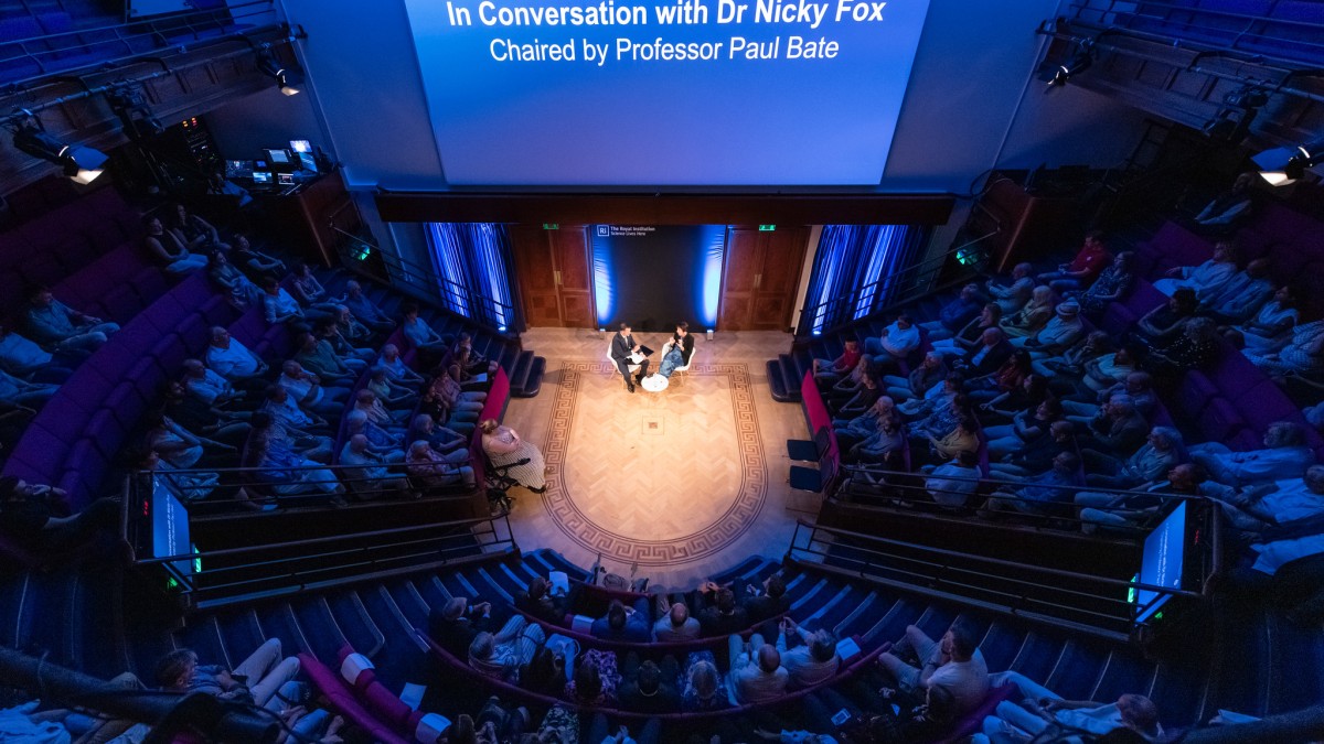 An aerial shot of the inside of the Royal Institution. A large audience watches an 'In Conversation' session with Professor Paul Bate and Dr Nicky Fox