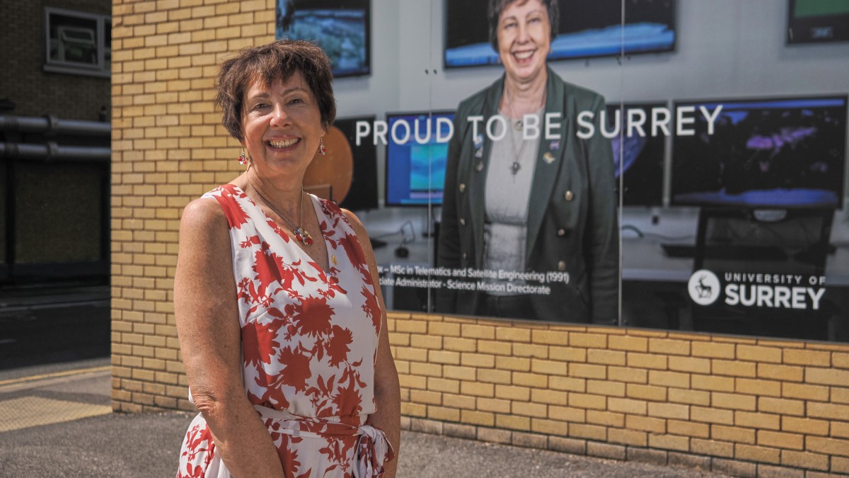 Dr Nicky Fox posing with her 'Proud to be Surrey' billboard on campus