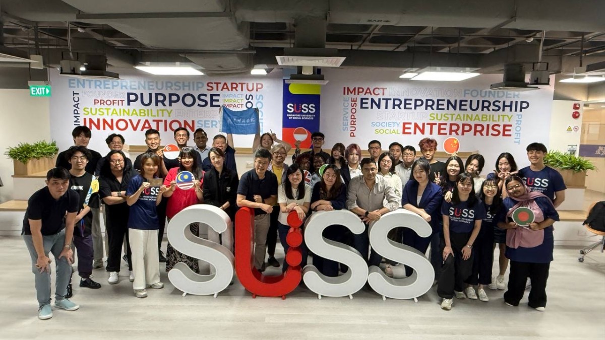 A group of people pose for a photo around large letters saying SUSS.