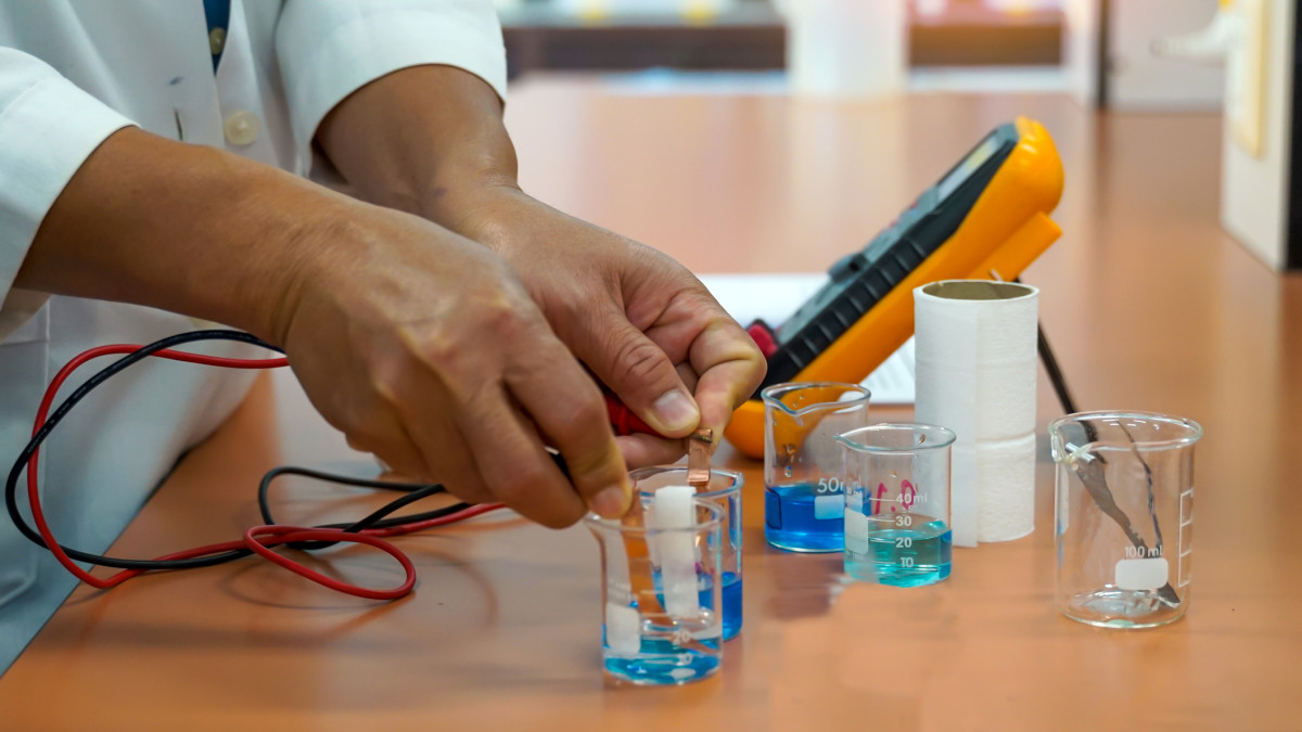 A student's hands measuring electrical currents between beakers