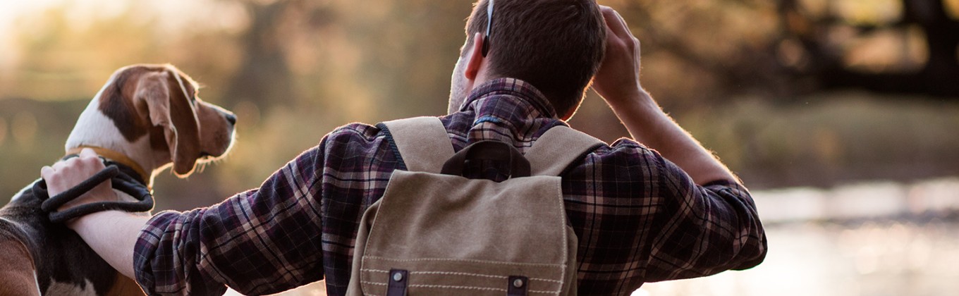 A man is patting a beagle next to a river